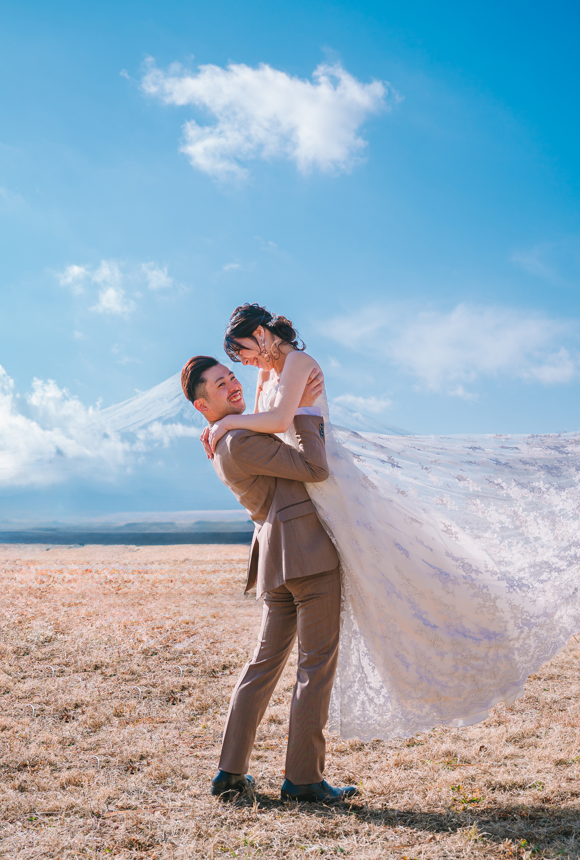 青空の下で新郎が新婦を抱き上げるウェディングフォト