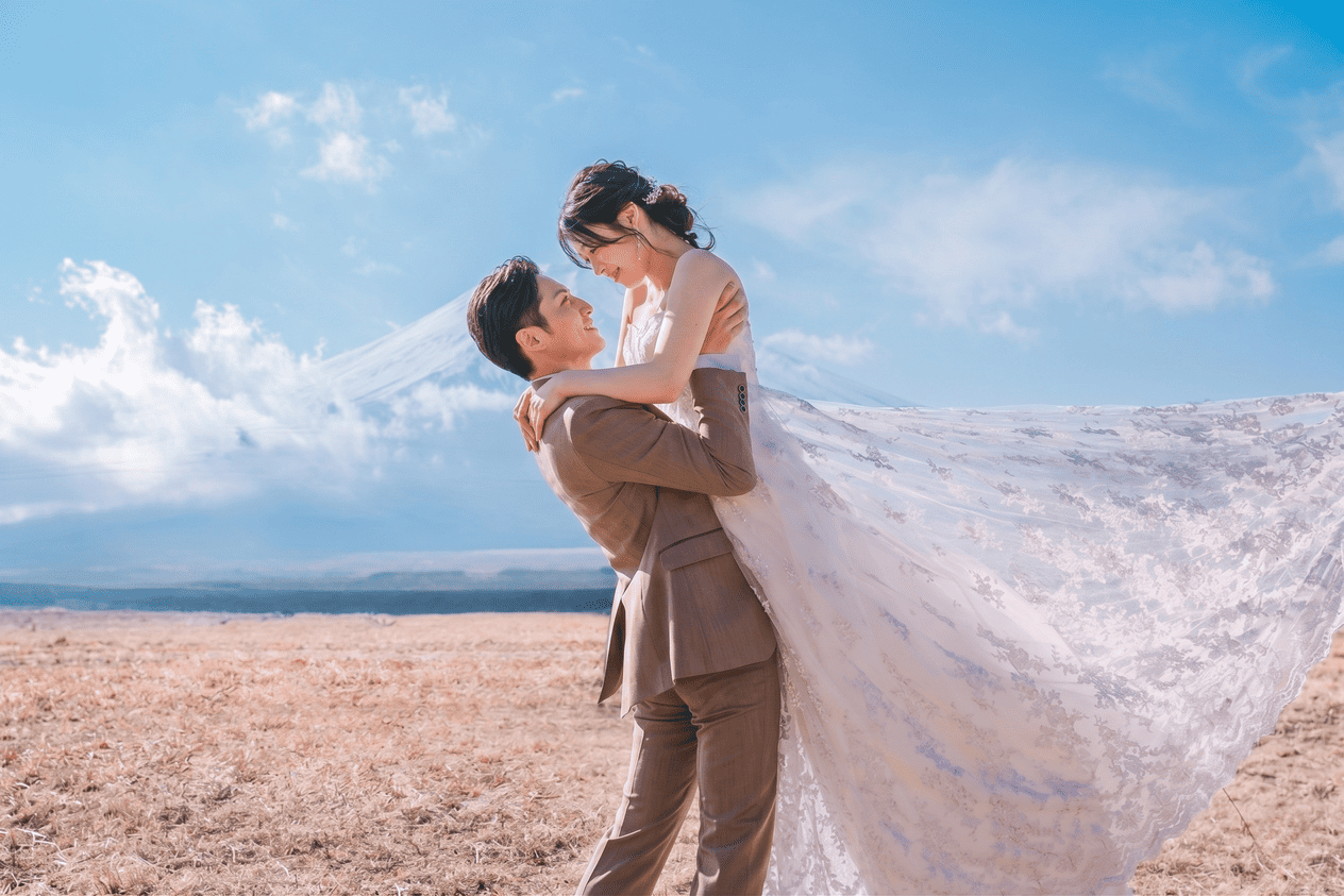 青空の下で新郎が新婦を抱き上げるウェディングフォト